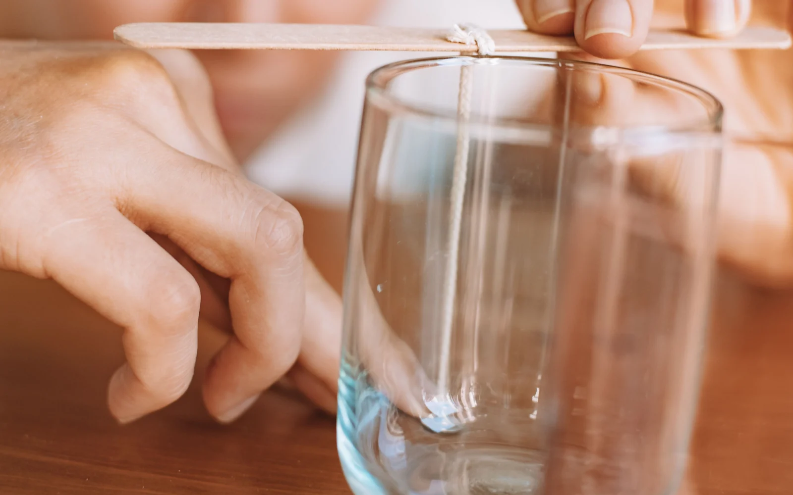 Hands positioning wooden wicks in clear glass candle jars during a candle-making process