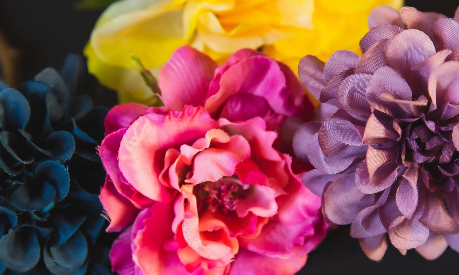 Assorted colourful artificial flower heads and stems against a dark background