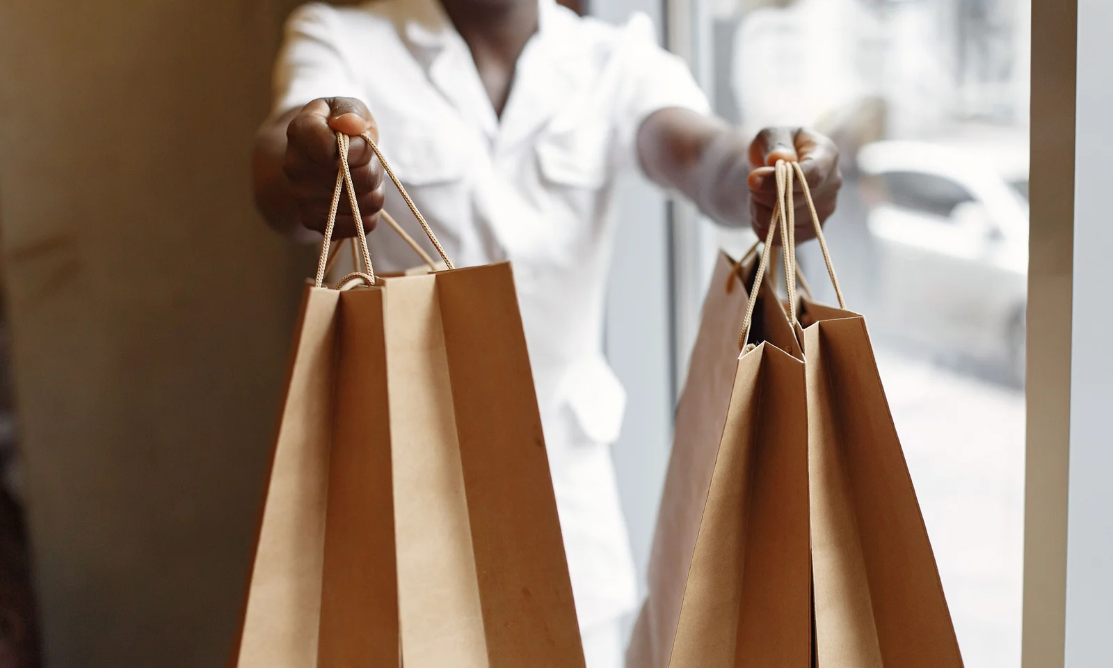 Retail worker handing several plain kraft paper bags with cord handles to a customer