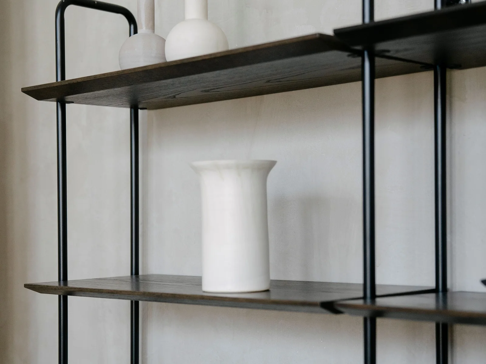 White sculptural vase displayed on a dark open shelf