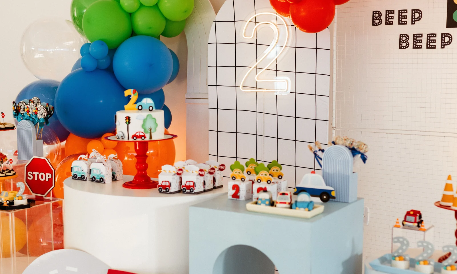 Car-themed birthday setup with balloons, backdrop, cake area and small props