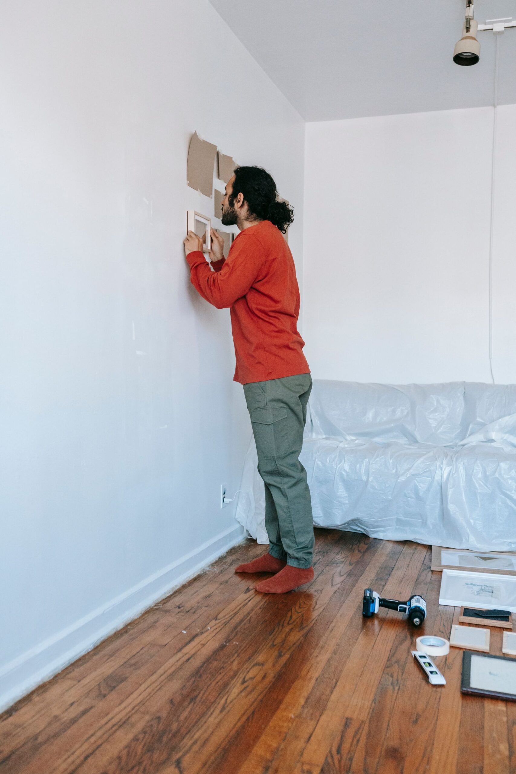 Person arranging framed wall art with a drill and level nearby