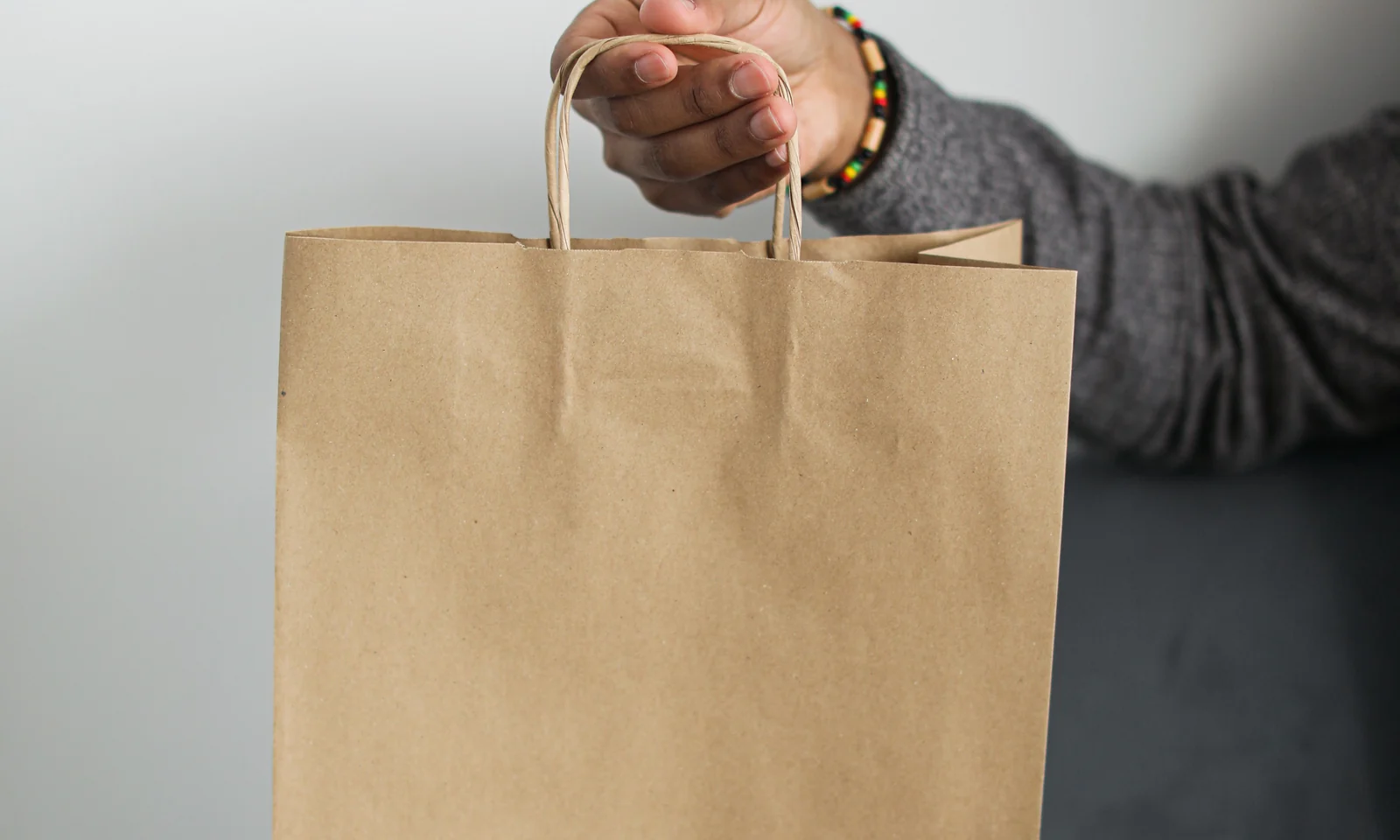 Hand holding a plain brown paper shopping bag by its paper handles