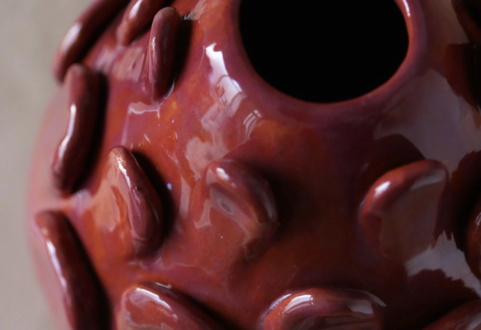 Close-up of a glossy red ceramic vase with raised decorative surface details