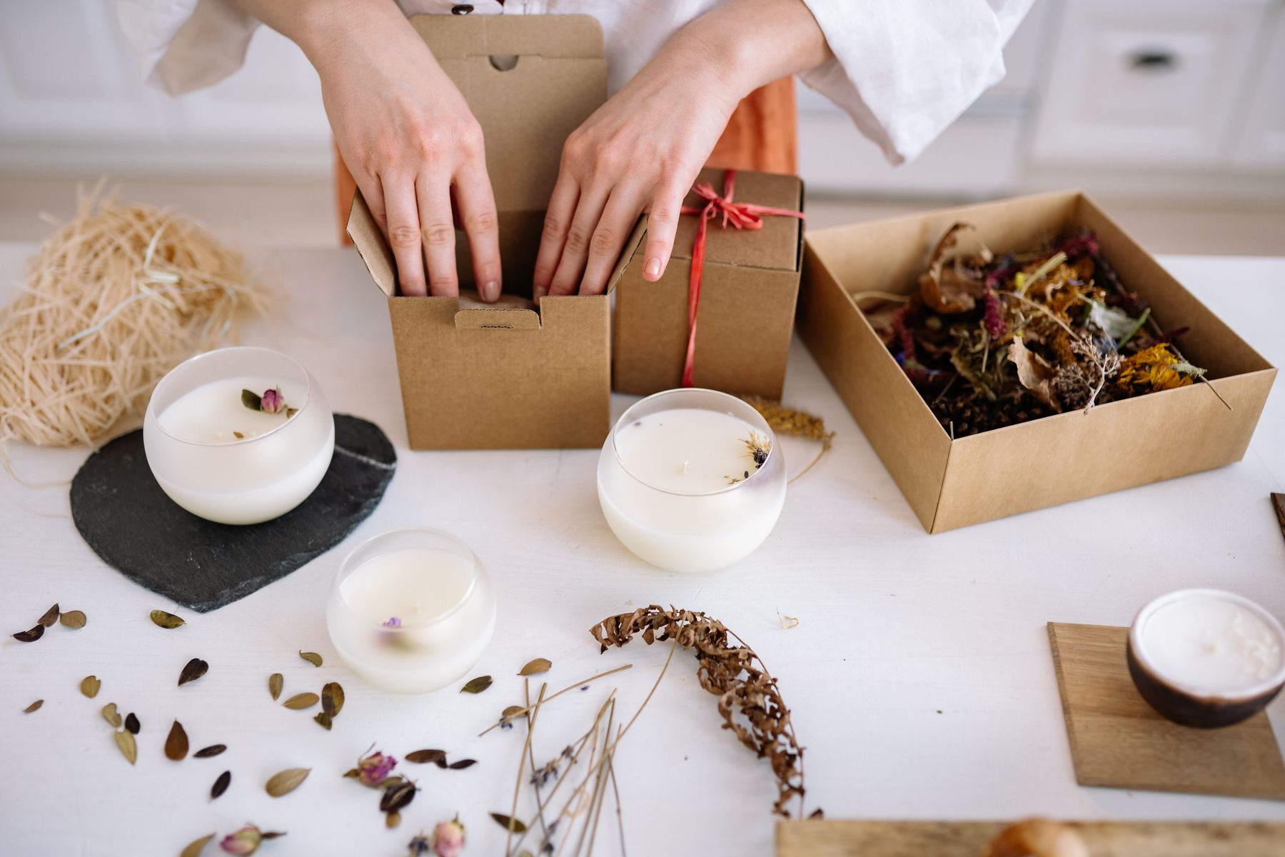 Hands packing decorative candles into kraft boxes with surrounding packing materials