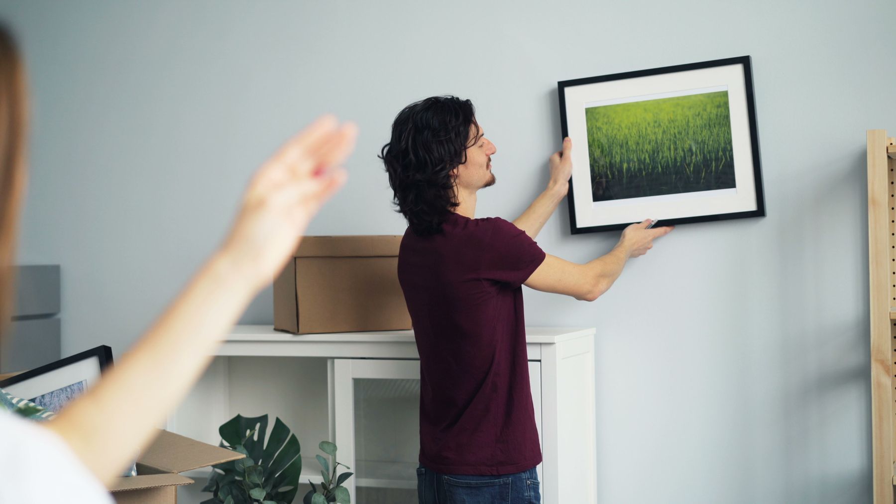 Person positioning framed art on a wall with moving boxes nearby