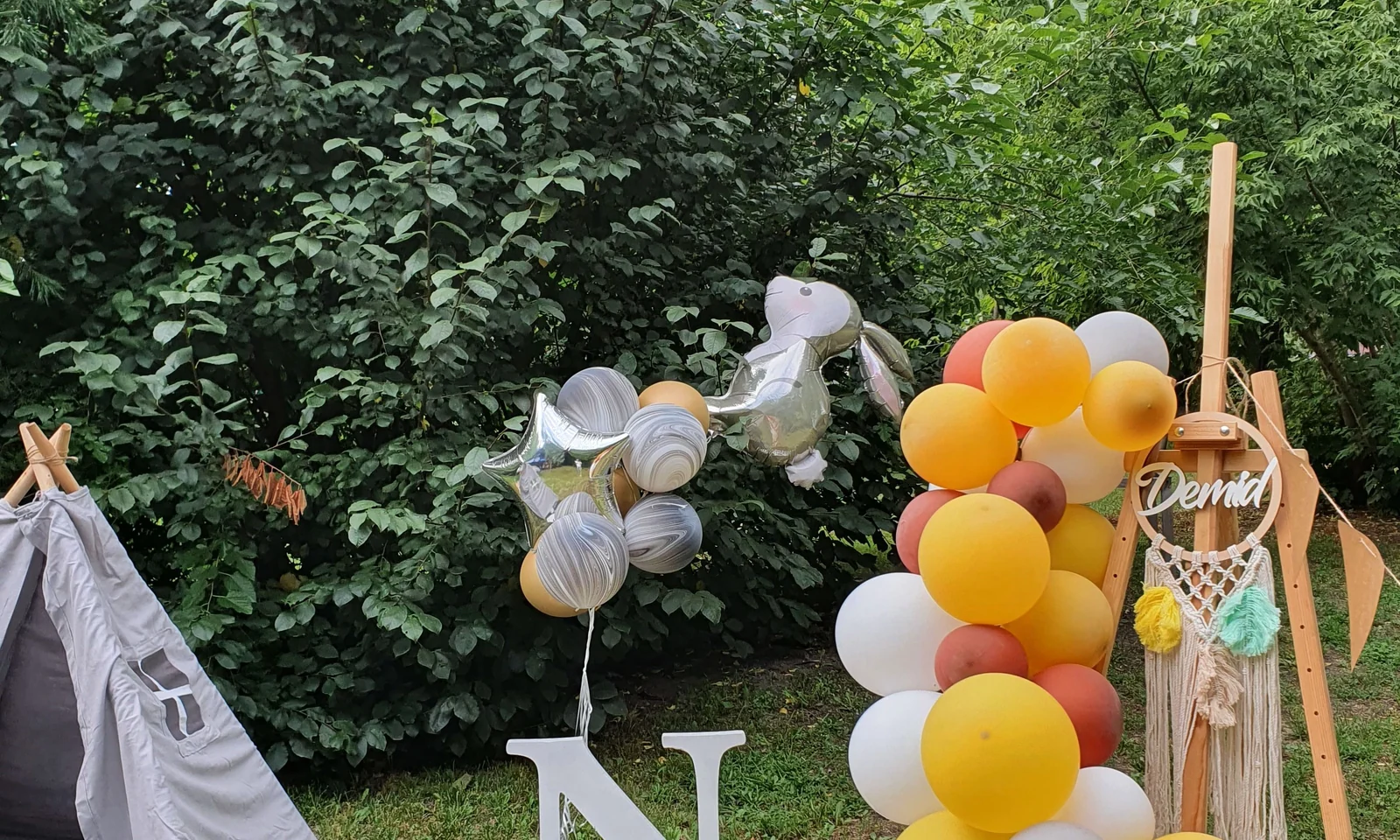 Outdoor birthday setup with balloons, sign, tableware and garden installation context