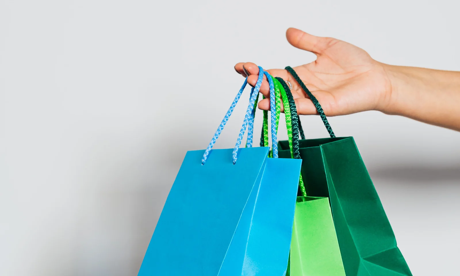 Hand holding several colourful paper shopping bags with different handles